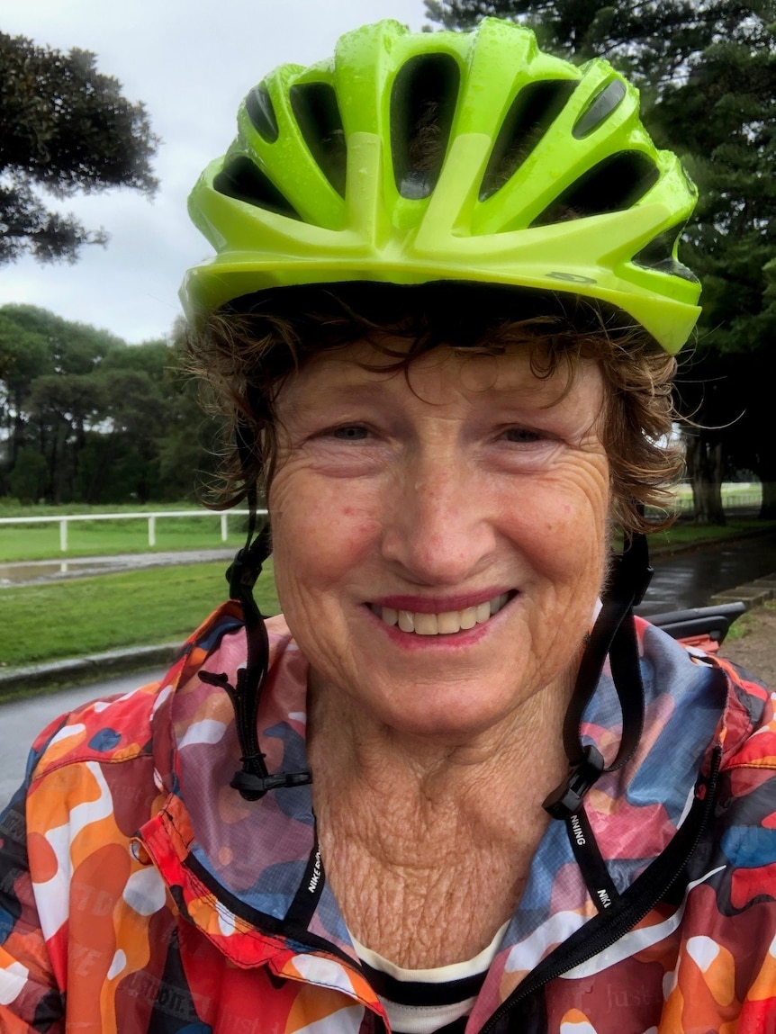 A close-up of an older woman wearing a neon green helmet and smiling to the camera.