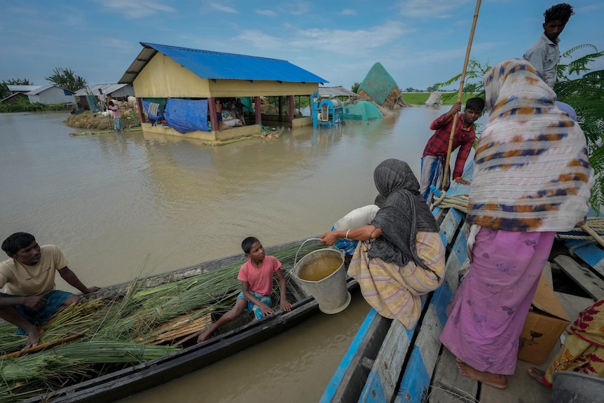 Women and children move from one canoe to another on top of a flooded farm area with a house visible
