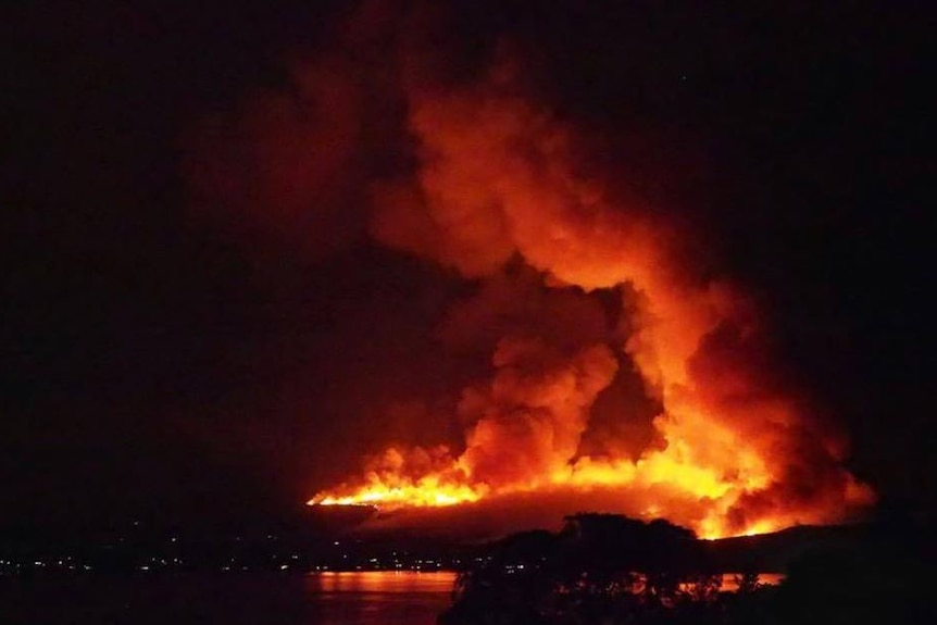 A wall of flame on a hill with lights in the foreground.