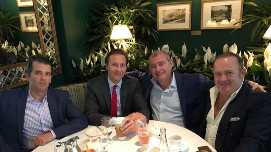 Donald Trump Jr, Tommy Hicks Jr, Lev Parnas and Igor Fruman sit around a table with food, green couch in background, smiling