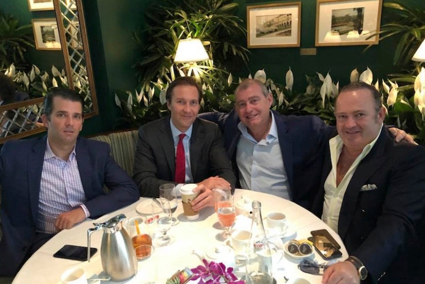 Donald Trump Jr, Tommy Hicks Jr, Lev Parnas and Igor Fruman sit around a table with food, green couch in background, smiling