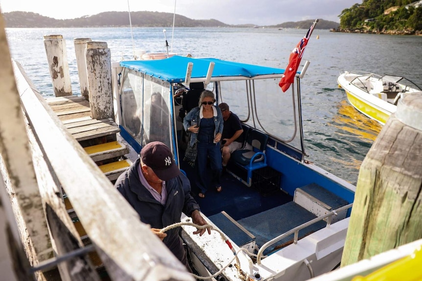 A photo of a man docking a water taxi to the wharf at Great Mackerel Beach. A woman is standing upright to disembark.