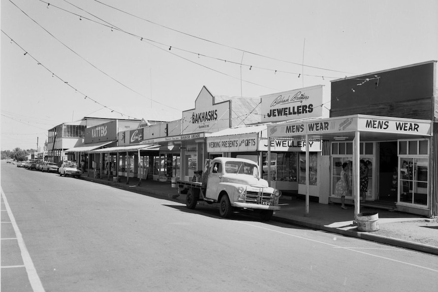 A black and white photo of a country strip in 1966 showing shops and old cars