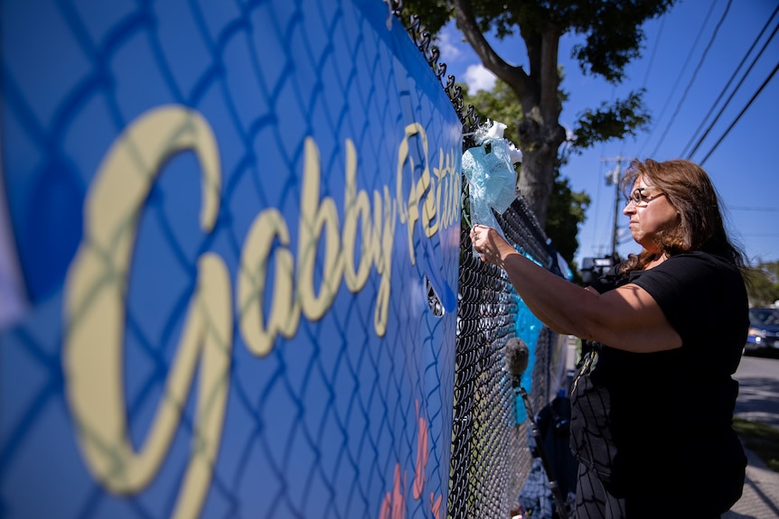A woman places flowers on a fence during Gabby Petito's memorial service