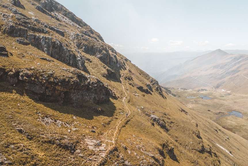 A rocky, grass-covered mountain with a thin walking track along it. 