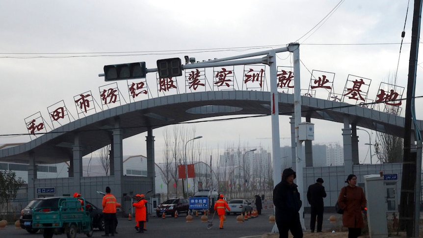 People wearing winter clothing walk past a concrete arch with red Chinese lettering on the top of it.