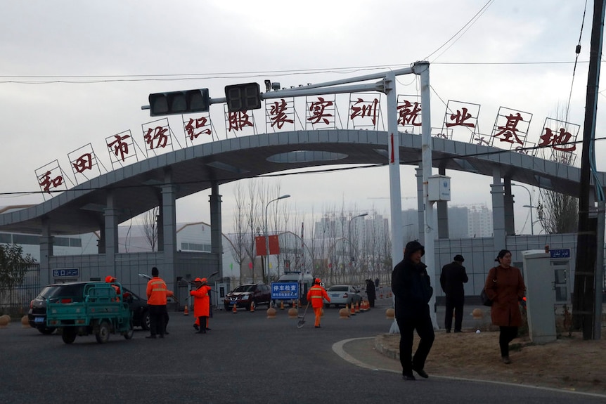 People wearing winter clothing walk past a concrete arch with red Chinese lettering on the top of it.