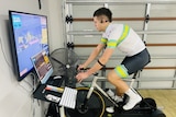 A cyclist on a stationary bike faces a screen in a garage.