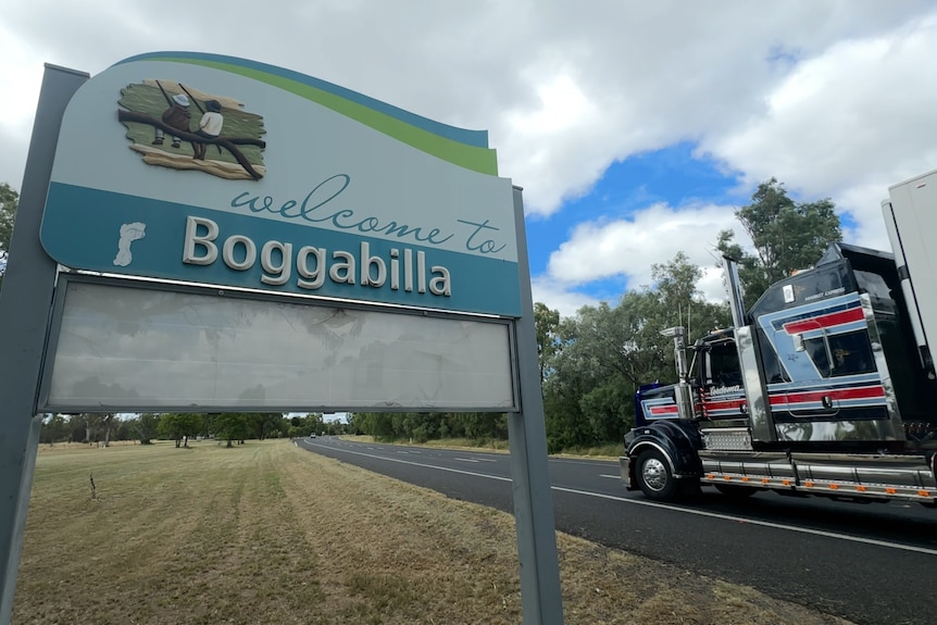 A welcome to Boggabilla sign stands next to the highway with a semi-trailer truck cruising by.