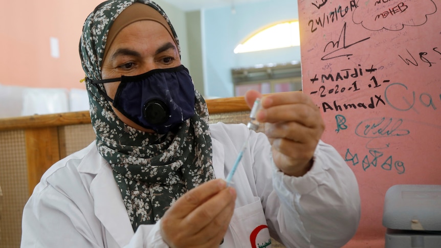 A Palestinian health worker prepares to give a member of education staff a dose of Sinopharm COVID-19 vaccine