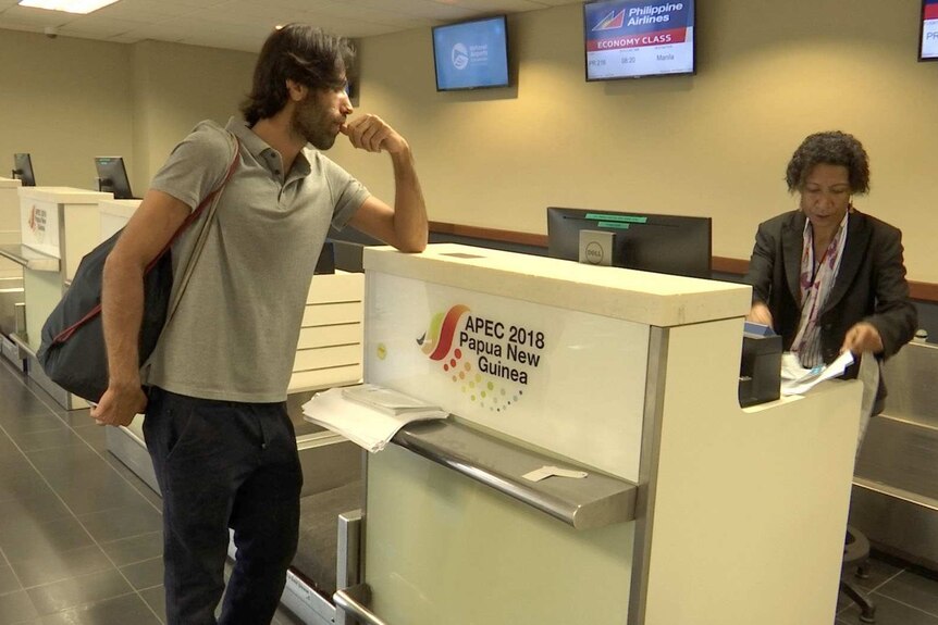 Behrouz Boochani leans on the counter at an airport check-in desk.
