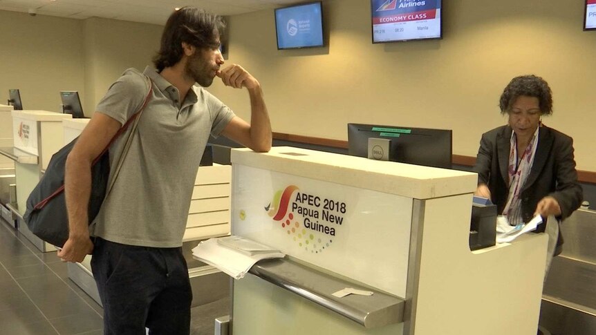 Behrouz Boochani leans on the counter at an airport check-in desk.