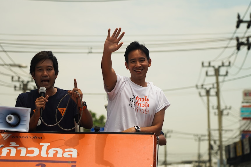 A man stands on the back of a truck waving to a crowd.