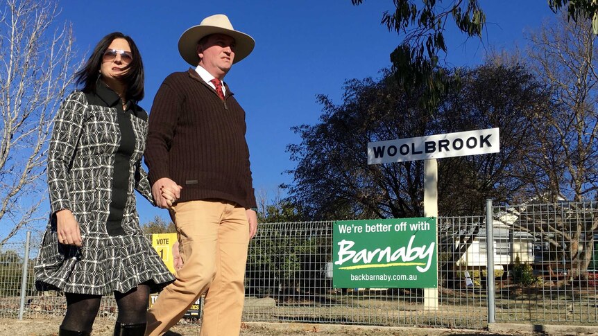 Barnaby and Natalie Joyce hold hands while walking past a 'Woolbrook' sign.