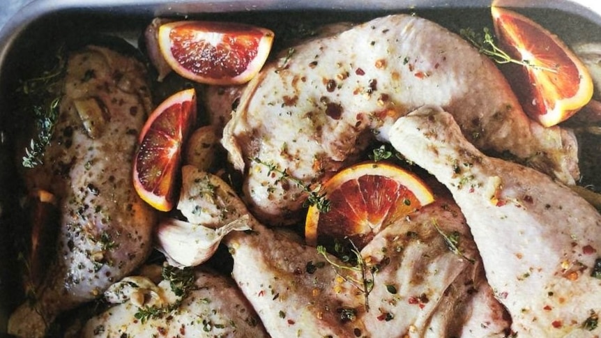 A metal pan of raw chicken marylands basted with olive oil and herbs, with slices of blood orange.