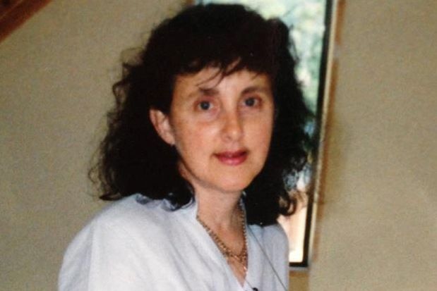 Medium close up of woman wearing white shirt looking into camera with a half-smile on her face. 