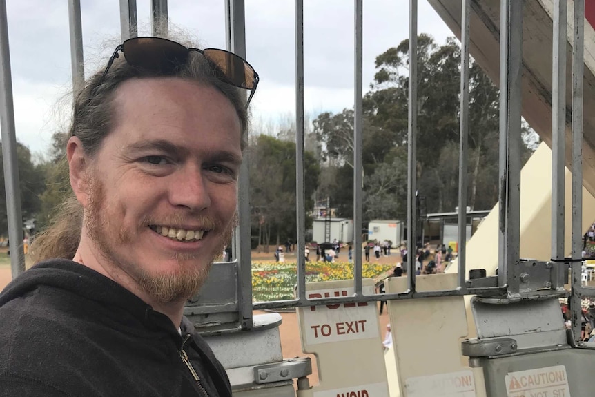 A photo of Chris Gough, he is smiling white standing on some industrial equipment that is overlooking a park.