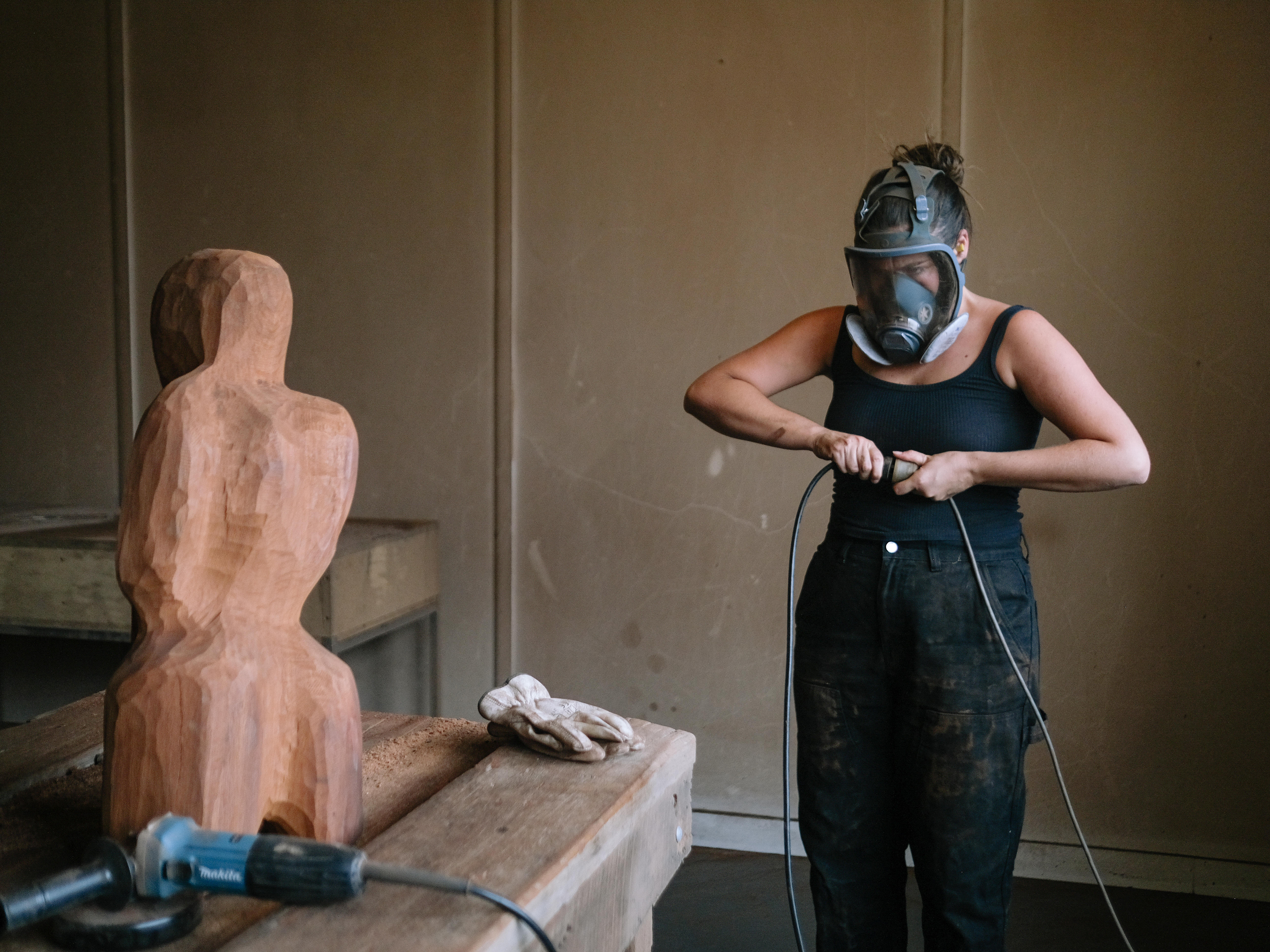 Womad with brown hair wearing black covered in wood dust after carving sculptures