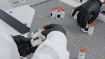 Inside a lab gloved hands are handling bottles of drugs