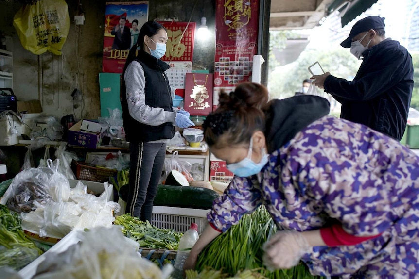 People wearing face masks buy vegetables at a street market in Wuhan, Hubei province,