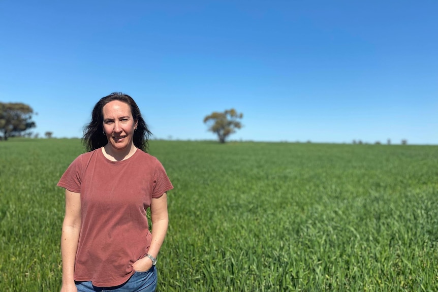 Woman stands in grassy field on a stunning clear day.