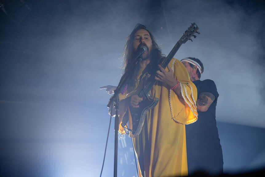 IDLES guitarist Mark Bowen wears a yellow dress while singing and playing on stage at Melbourne's Festival Hall