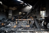 The gutted interior of a home destroyed in a bushfire, with beams and furniture and other items charred and scattered around.