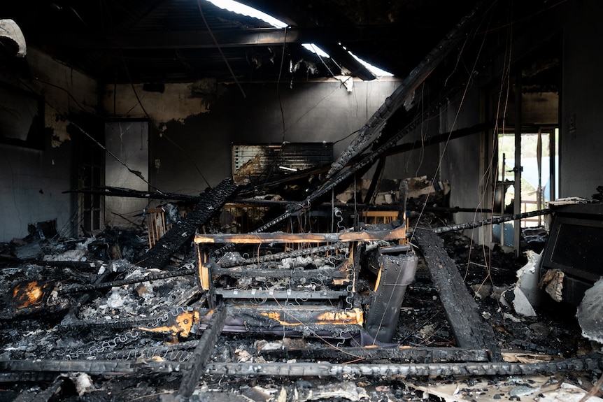 The gutted interior of a home destroyed in a bushfire, with beams and furniture and other items charred and scattered around.