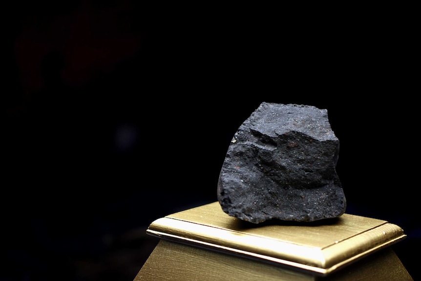 A chunk of grey rock sits on a wooden plinth.