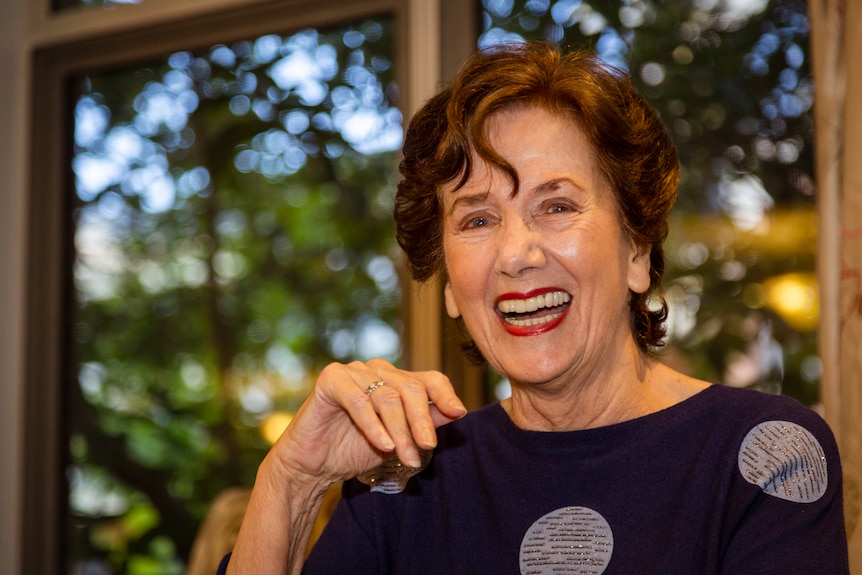 Maureen looks into the camera laughing wearing a blue top with sparkly white polka dots on it.