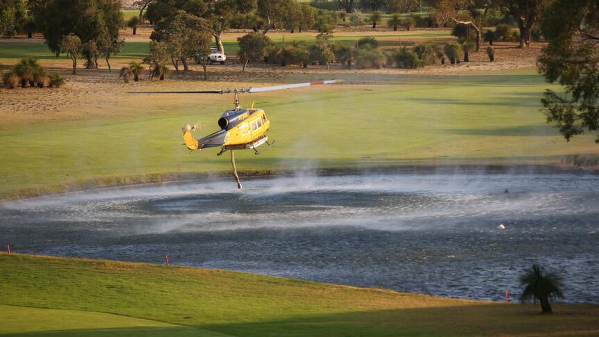 A water bomber sucks up water at a golf course lake