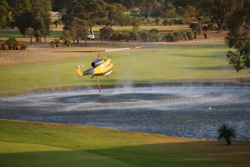 A water bomber sucks up water at a golf course lake