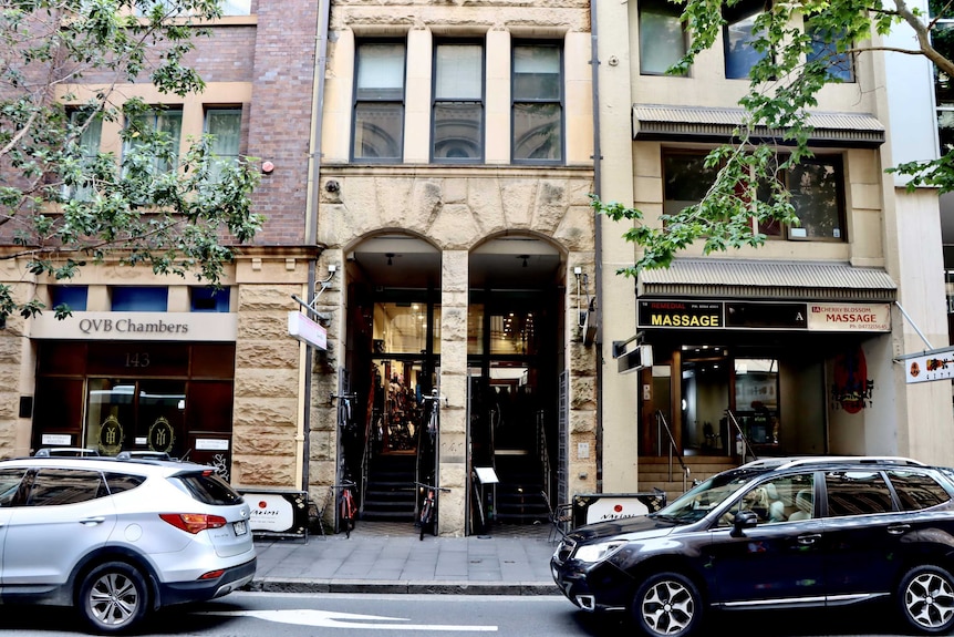 A sandstone fronted office building with two cars parked on the street in front of it.