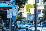 Parking signs in a street packed with cars at West End in inner-city Brisbane, among them is a disability parking sign