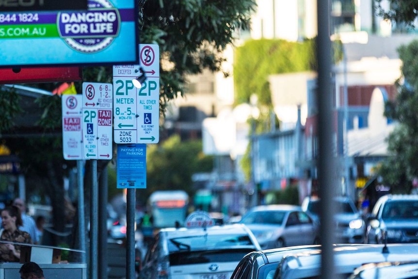 Parking signs in a street packed with cars at West End in inner-city Brisbane.