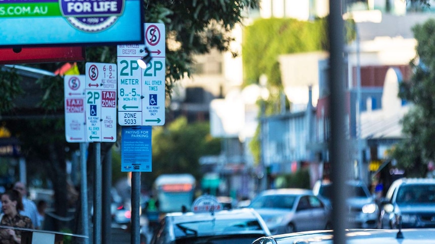 Parking signs in a street packed with cars at West End in inner-city Brisbane.