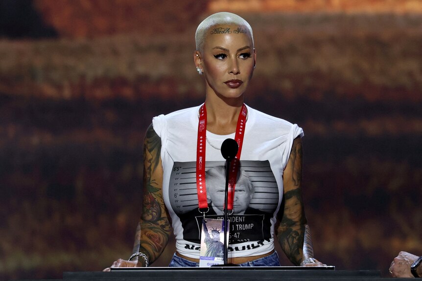 Amber Rose stands at a podium with a Donald Trump mugshot displayed on a white t-shirt.