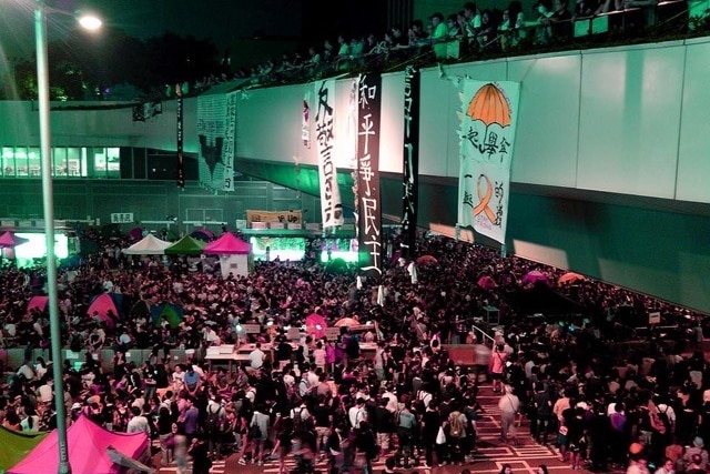 An aerial view of a crowd of people gathering in a public space. There are some banners hanging from the wall.