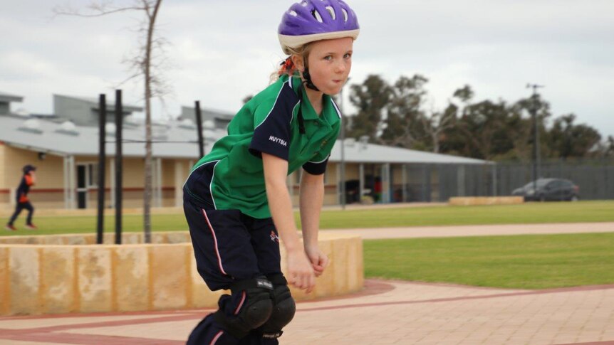 A young student rollerblades along a path at Honeywood Primary School wearing a purple helmet and green shirt.