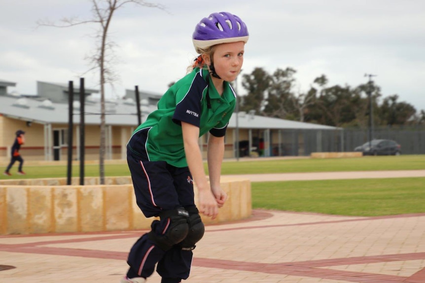 A young student rollerblades along a path at Honeywood Primary School wearing a purple helmet and green shirt.