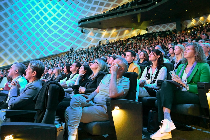 An audience of people looking on with faces focused on stage