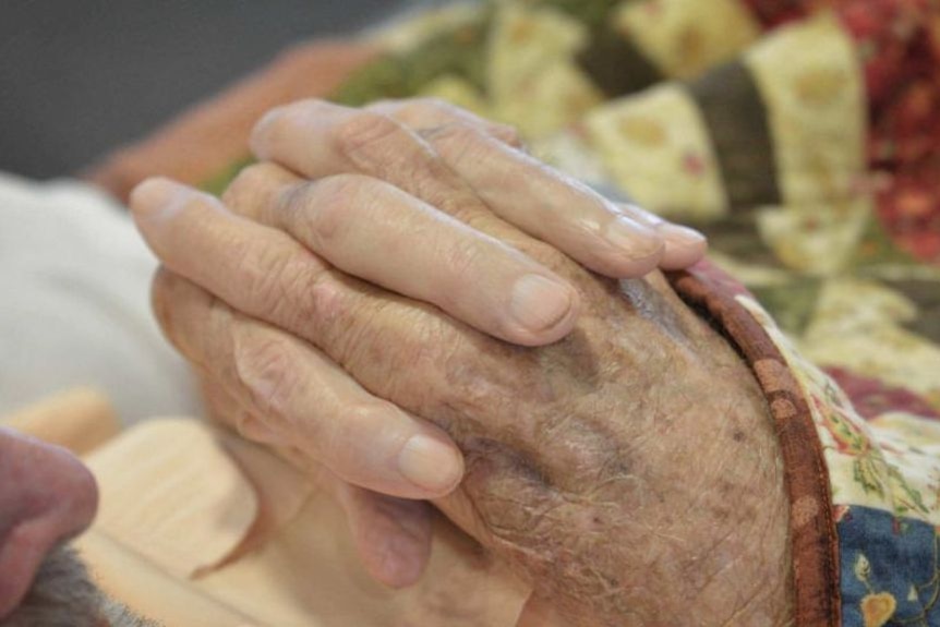 A close up of hands are held together by two elderly people.