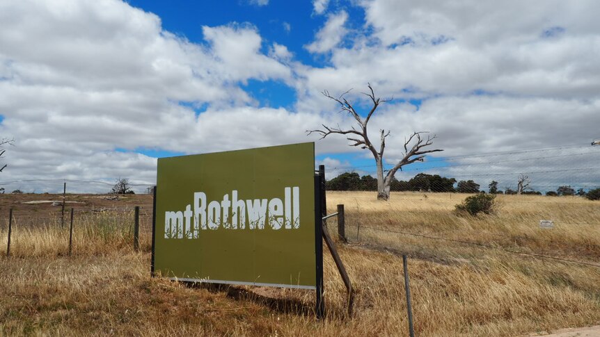 A green billboard with the words "Mt Rothwell" on it sits in a paddock of dry grass.