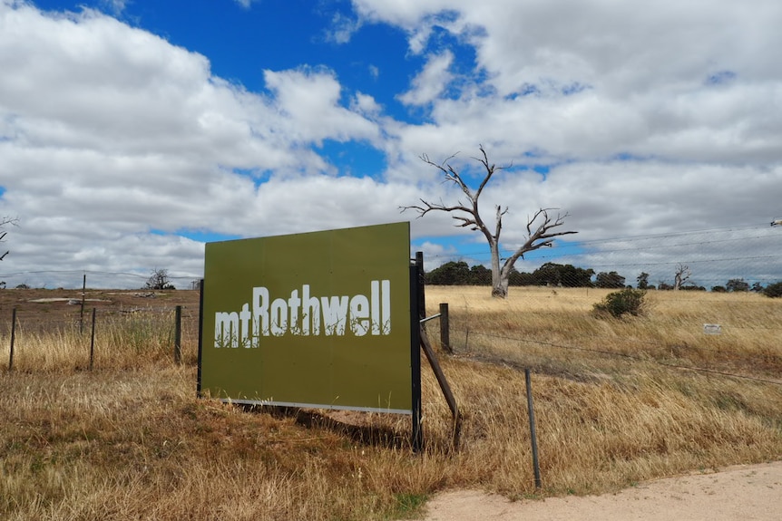 A green billboard with the words "Mt Rothwell" on it sits in a paddock of dry grass.