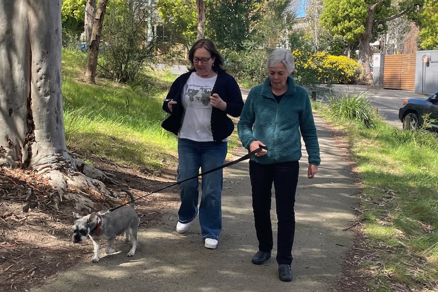 Alison Read walking wearing a blue jumper with her mum Lyn on her left. Lyn and Alison are walking the dog in a park.