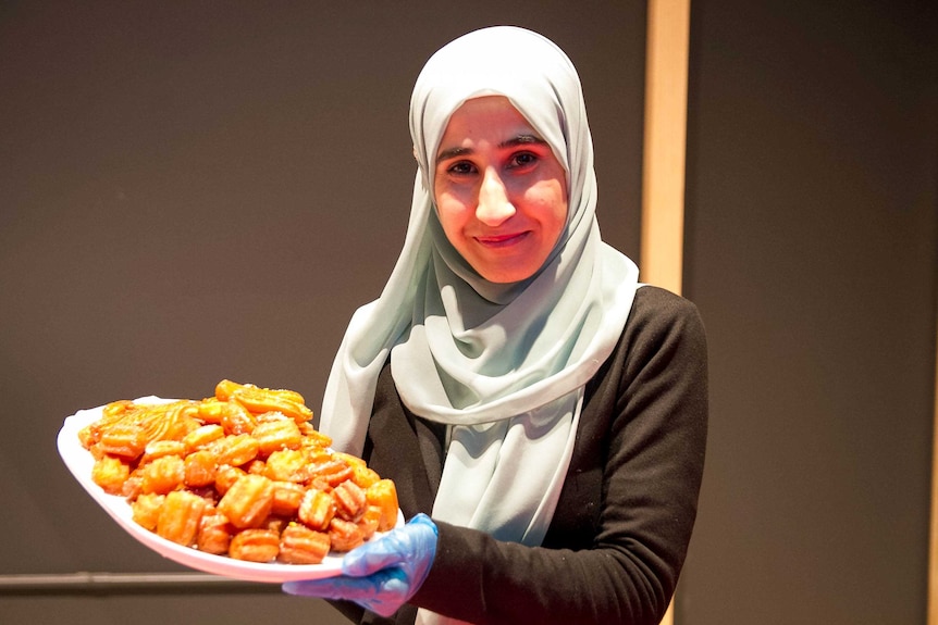 A young woman holds a tray of Middle Eastern deep fried sweets.