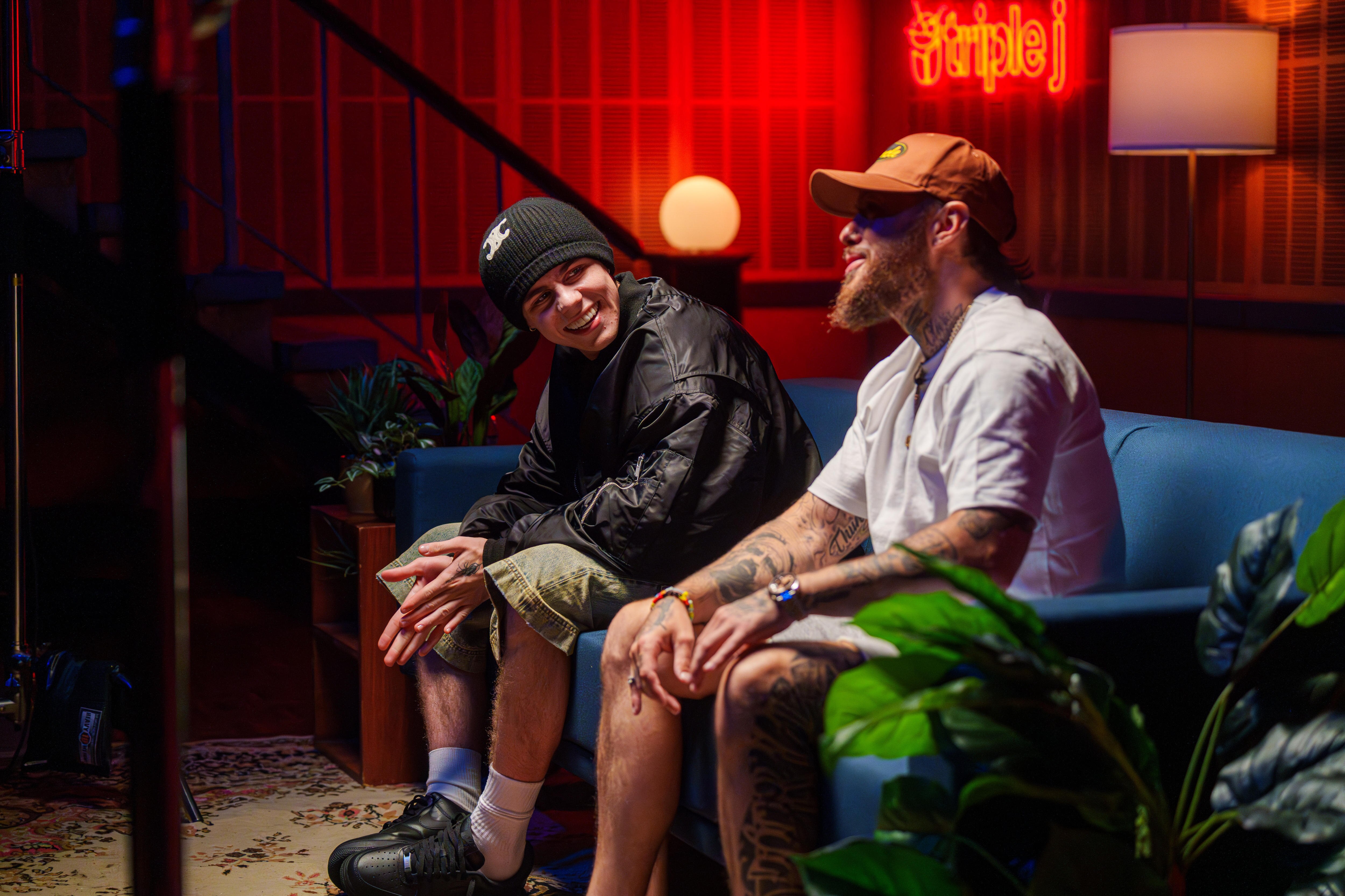 The Kid LAROI and Nooky sit together on a blue couch in a darkened room