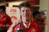 A football player in a red shirt holds up a medal that is around his neck