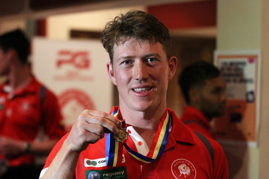 A football player in a red shirt holds up a medal that is around his neck