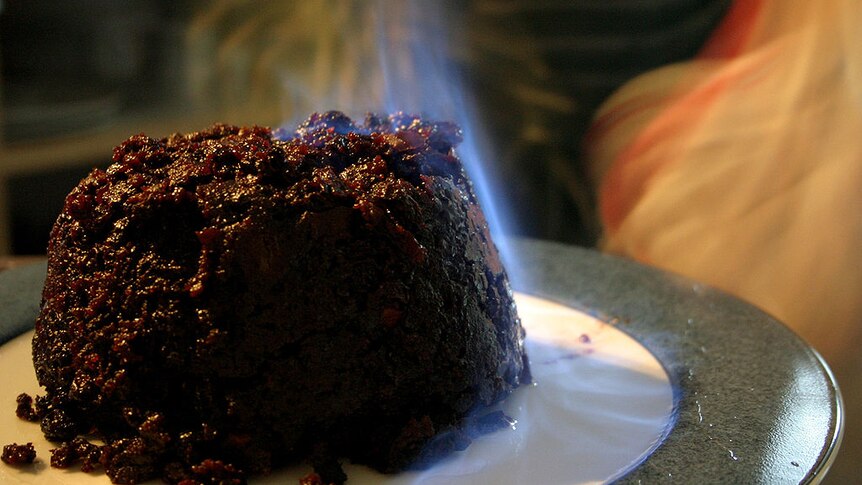 Plum pudding on a plate, with a slight blue flame (flambe) on the pudding.